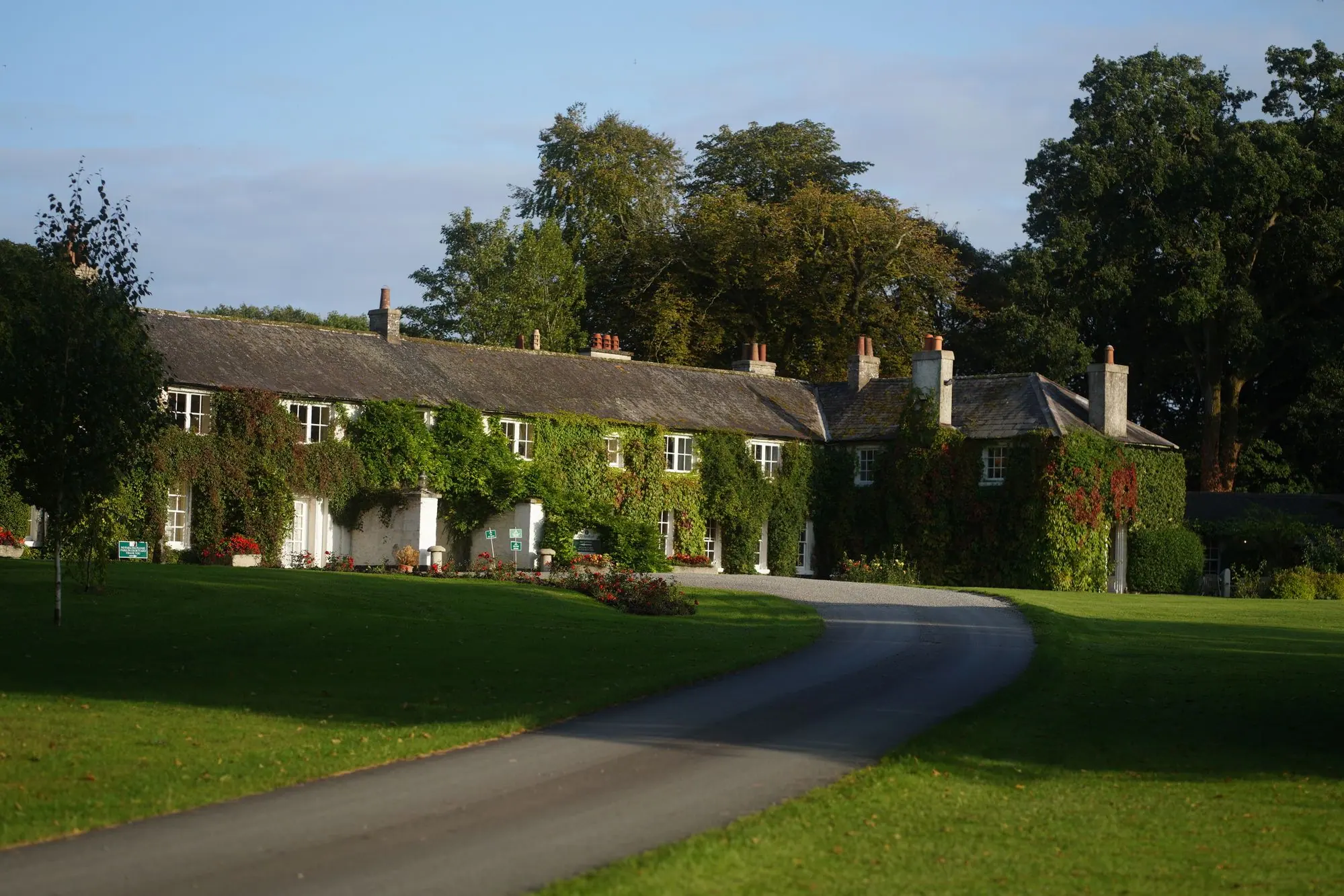 An ivy covered country house at golden hour, with a gravel drive curving across the lawn
